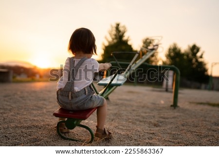back view of one small caucasian toddler child sitting alone on the seesaw in park in sunset lonely with no friends copy space childhood growing up concept social issues rejected Royalty-Free Stock Photo #2255863367