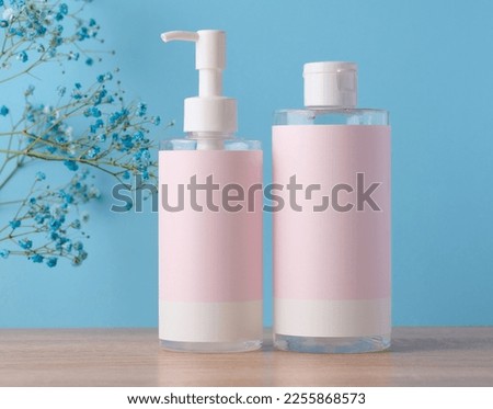 Two bottles for cosmetics with a pink paper label on a blue background. Bottle for tonic, gel