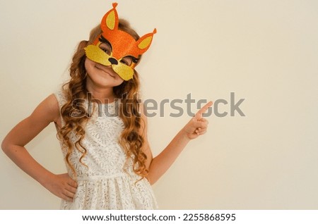 A child in a carnival masquerade mask of a squirrel made of shiny foamiran. The child is fooling around in carnival masks. The mask is handmade. Girl getting ready for the carnival or masquerade. 