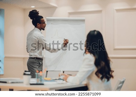 Diverse colleagues gathered in the office having fun during brainstorming while discussing new ideas for their new project. Focus on an arabic muslim businessman writing stats on a flipchart.