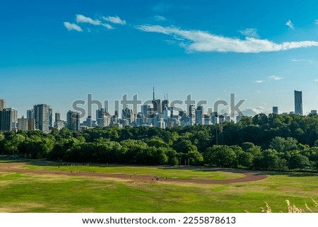 Toronto skyline at warm summer. Toronto, Ontario, Canada. Panoramic view of Toronto skyline near Ontario lake at sunset at scattered clouds. People playing in Riverdale Park