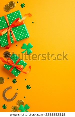 St Patrick's Day concept. Top view vertical photo of green gift boxes with orange bows trefoils shamrock shaped confetti horseshoe and gold coins on isolated yellow background with empty space