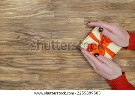 Female woman hands in yellow sweater holding craft paper gift present box on wooden background,Christmas New Year decoration with copy space.Flat lay mockup.Festive template background.