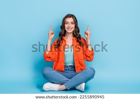 Full body photo of young lovely lady sitting floor point up empty space dressed stylish orange clothes isolated on blue color background