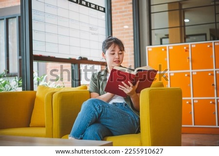 female college student is reading a book in a cafe during the day.
