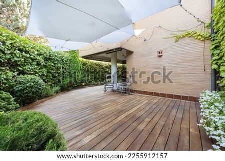 Terrace of a ground floor house with hedges and ornamental plants, slatted acacia hardwood floors twin wooden sunbeds and white awnings Royalty-Free Stock Photo #2255912157