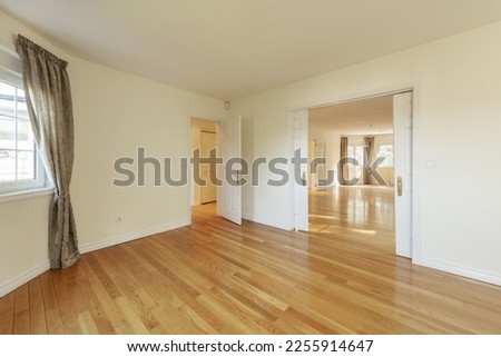 Dining room of a spacious empty house with wooden floors, sliding double doors, windows with curtains and access to multiple rooms