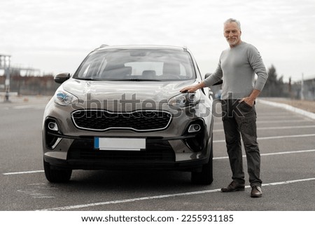 Full length portrait of a handsome imposing 60-70 years old senior man smiling at camera, standing near his newly bought luxury car, in the outdoors parking lot. Looking for new comfortable automobile Royalty-Free Stock Photo #2255931185