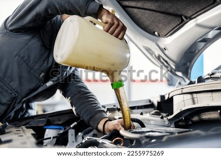 Close up picture of a mechanic pouring oil in engine under the hood while standing at mechanic's workshop.