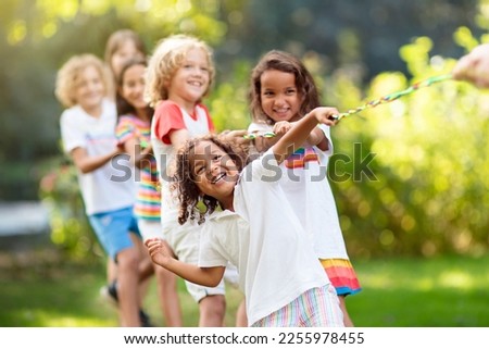 Kids play tug of war in sunny park. Summer outdoor fun activity. Group of mixed race children pull rope in school sports day. Healthy outdoor game for little boy and girl. Royalty-Free Stock Photo #2255978455