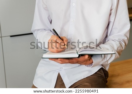 Business man in the workplace does records in a diary. Blank book page copy write a message. Young woman right hand writing plans on small diary. Businessman in suit at workspace make thoughts records