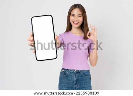 Cheerful beautiful Asian woman holding big smartphone and shows ok sign on grey background. Royalty-Free Stock Photo #2255988109
