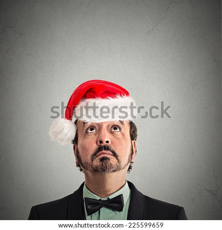 closeup headshot xmas man with red santa claus hat looking up at copy space on grey wall background thinking of gift idea for holiday.  Human face expression emotion perception reaction