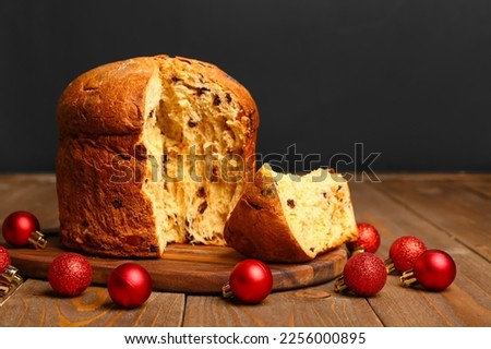Board with cut Panettone and Christmas balls on table against black background