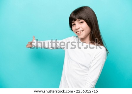 Little caucasian girl isolated on blue background extending hands to the side for inviting to come