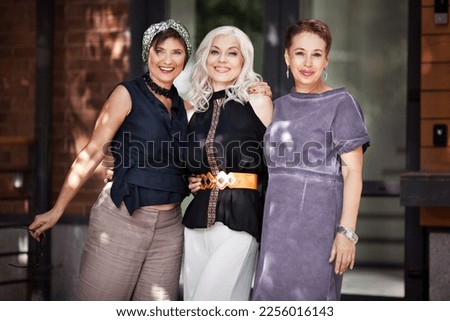 Mature women hug and look at camera on city street. Portrait of happy middle age friends outside. Female friendship Royalty-Free Stock Photo #2256016143