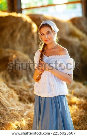 Beautiful blonde smiley girl with braided hair in white rural clothes standing on a straw background. Farm life.Young model posing on a ranch.Warm art work.