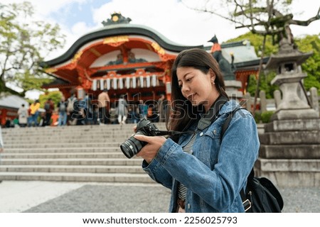 attractive asian chinese girl photographer checking photos in slr camera with the worship hall of Fushimi Inari Taisha shrine at background in Kyoto japan