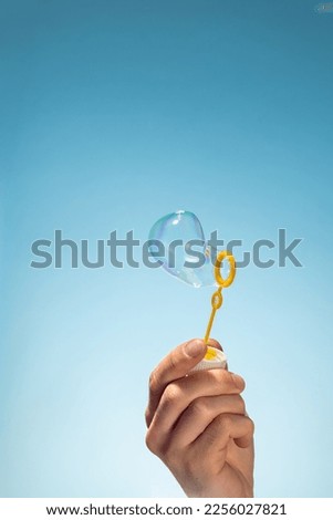 Close up side view shot of young man blowing soap bubbles on blue background. Focus on hand and wand.
