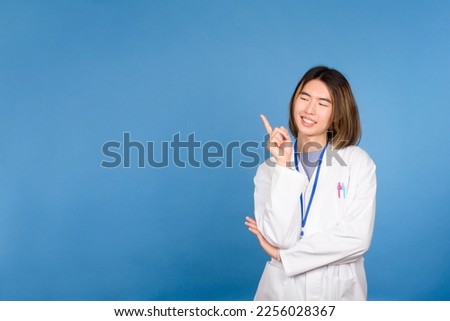 Studio portrait with blue background of an asian doctor pointing up to a blank space