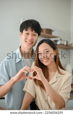Portrait, Lovely young Asian couple making a heart hand sign together in the kitchen, smiling and looking at the camera. happy relationship, girlfriend and boyfriend