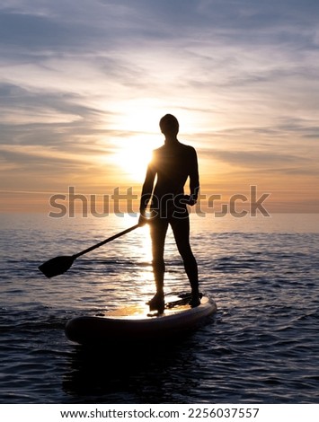 a sporty guy swims with a paddle on a sapboard in the sea under the beautiful sunset sun Royalty-Free Stock Photo #2256037557