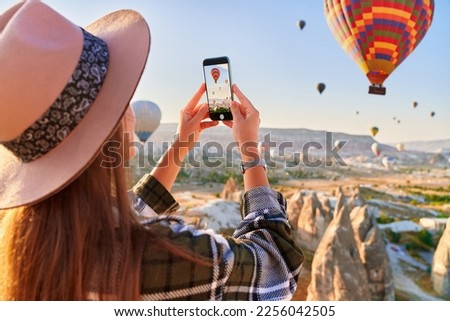 Girl tourist vacations in beautiful destination in Goreme, Turkey. Taking photo of flying air balloons in fabulous Kapadokya at sunrise, Anatolia