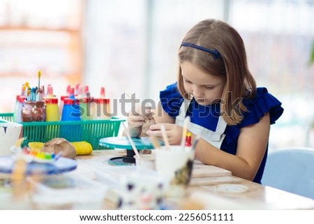 Child working on pottery wheel. Kids arts and crafts class in workshop. Little girl creating cup and bowl of clay. Creative activity for young children in school. Cute kid forming toy with ceramic.  Royalty-Free Stock Photo #2256051111