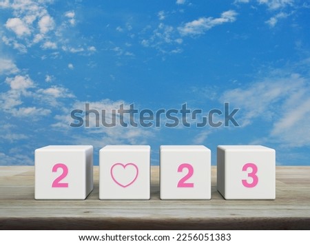 Love icon with 2023 letter on white block cubes on wooden table over blue sky with white clouds, Happy new year 2023 and Valentines day concept