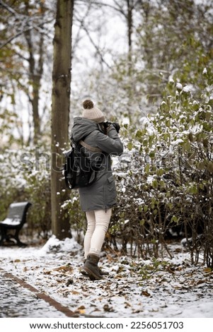 Unrecognizable woman photographer taking pictures in the snowy Tiergaten Park in Berlin - tourism and photography concept
