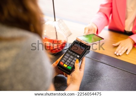 Croped young smiling fun happy woman wearing pink shirt hold wireless bank payment terminal to process acquire credit card sit alone at table in coffee shop cafe restaurant indoor. High quality photo