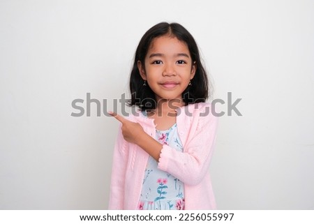 Asian little girl smiling at the camera and pointing finger to the right side