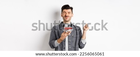Happy birthday guy making wish on cake with candle, celebrating bday, standing on white background.
