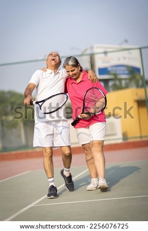 Senior man and woman hugging after playing a game of tennis at an outdoor court.