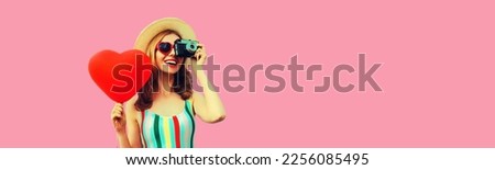 Summer portrait of happy smiling young woman with film camera and red heart shaped balloon wearing straw hat on pink background, blank copy space for advertising text