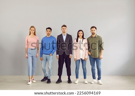 Group portrait of young people in smart casual clothes. Team of 5 unsmiling corporate employees in jumpers, jackets, shirts, trousers and jeans standing in studio. Work dress code in office concept Royalty-Free Stock Photo #2256094169