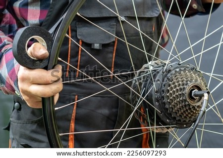 The bike mechanic holds in his hand the rear wheel of the electric bike and the rim tape. Protection of the bicycle camera from punctures, cuts and friction. Professional bicycle repair.