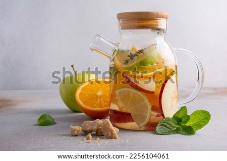 Homemade healthy hot fruit tea with fresh ripe orange, apple, mint leaves and twigs of thyme in glass teapot or kettle on grey kitchen background Royalty-Free Stock Photo #2256104061
