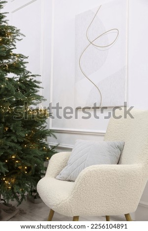 Stylish armchair near beautiful Christmas tree decorated with festive lights indoors