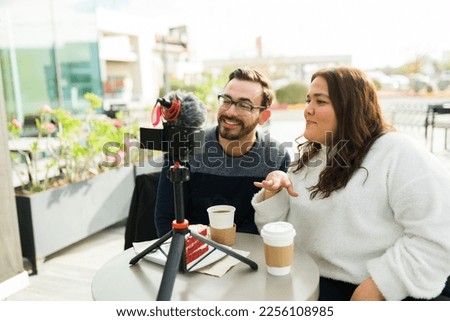 Happy influencer couple filming for their social media content and talking to the camera while smiling at a coffee shop