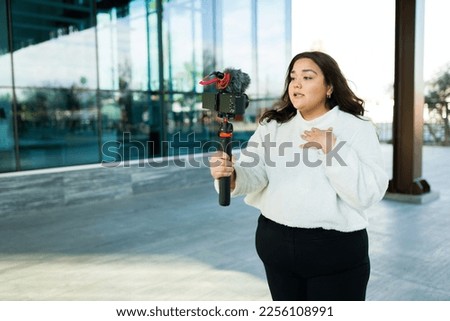 Attractive big woman using a camera and stabilizer to film a video blog and making social media content