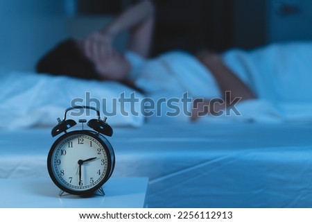 Close-up alarm clock on the table have a sleepless woman as background Royalty-Free Stock Photo #2256112913