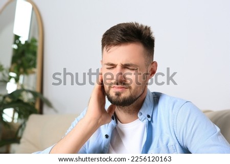 Young man suffering from ear pain at home. Space for text Royalty-Free Stock Photo #2256120163