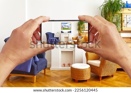 Augmented or mixed reality concept: hands holding smart phone with AR interior decoration app, visualizing the living room with an added poster print.