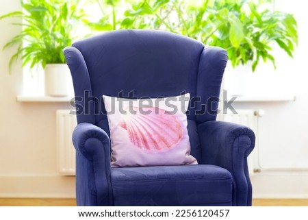 Customisable products concept: retro blue wingback chair with a customized throw pillow with the print of a pink shell picture.