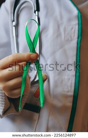 the doctor holds a green ribbon in his hands