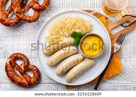 German food. Top view. Bavarian white sausage Weisswurst made from minced veal and pork back bacon, crauti or sauerkraut, mustard and a soft pretzel. Royalty-Free Stock Photo #2256128609