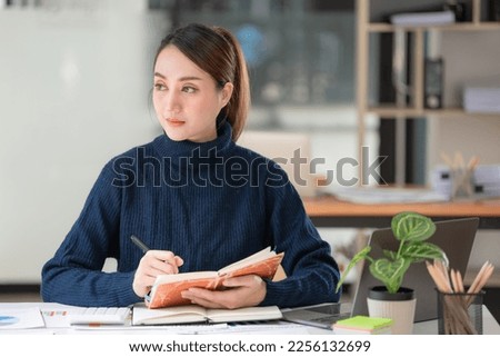 Asian businesswoman think and write in notebooks during working on a laptop in an office.