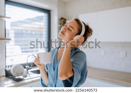 Young woman listening music and enjoying cup of coffee at morning, in her kitchen. Royalty-Free Stock Photo #2256140573