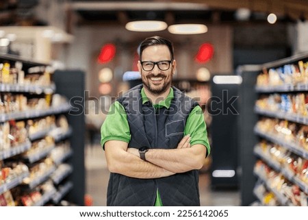A proud supermarket seller is standing with arms crossed at marketplace and smiling at the camera. Royalty-Free Stock Photo #2256142065